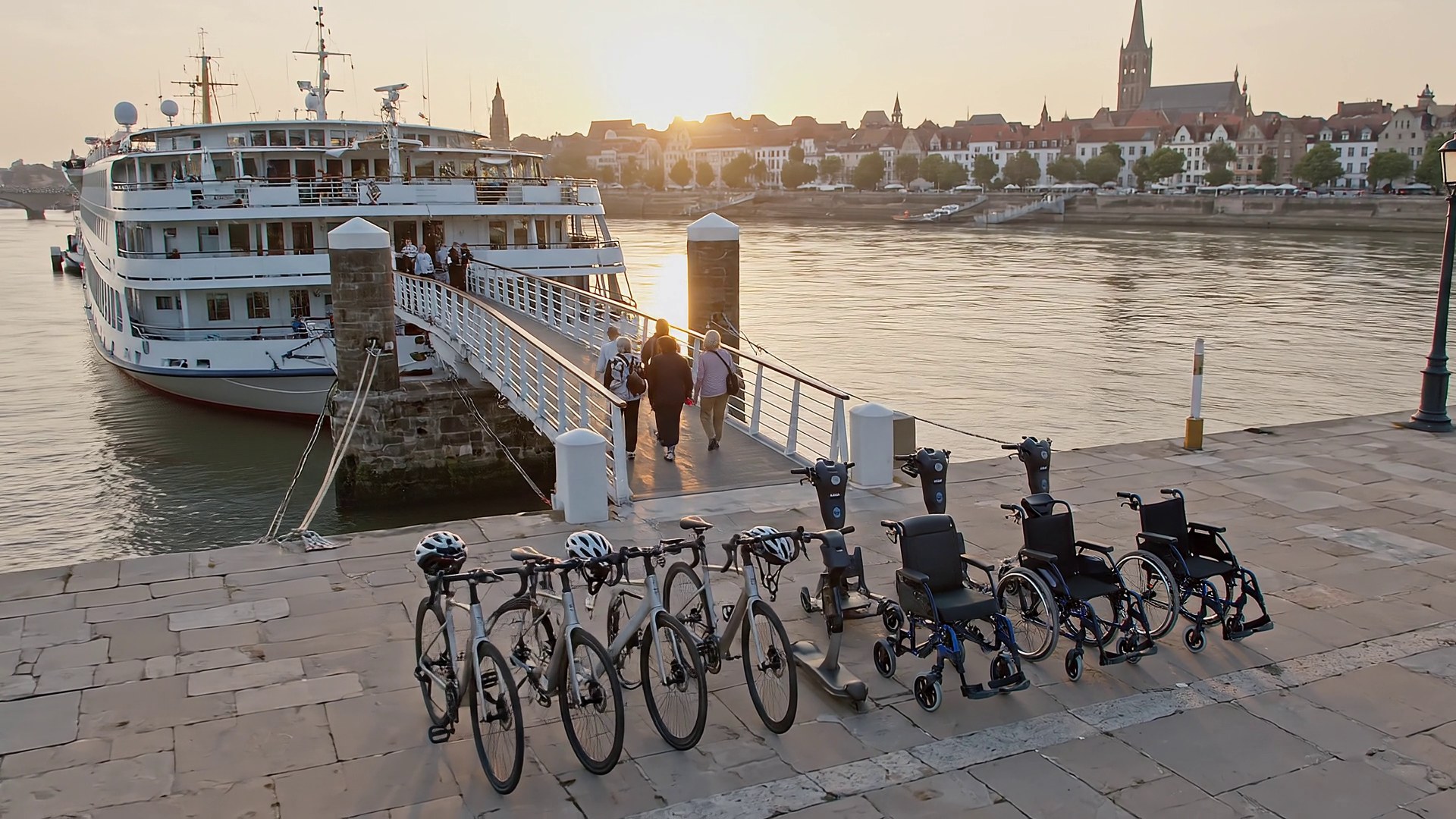 Bikes and wheelchairs staged on a quay beside a river cruise ship at sunset